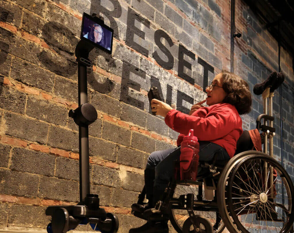 A person using a robot to join remotely speaks with a person using a wheelchair.