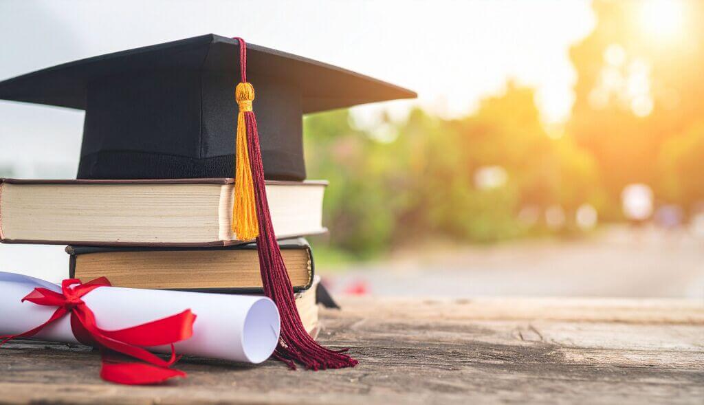 graduation cap on top of books and with diploma close by