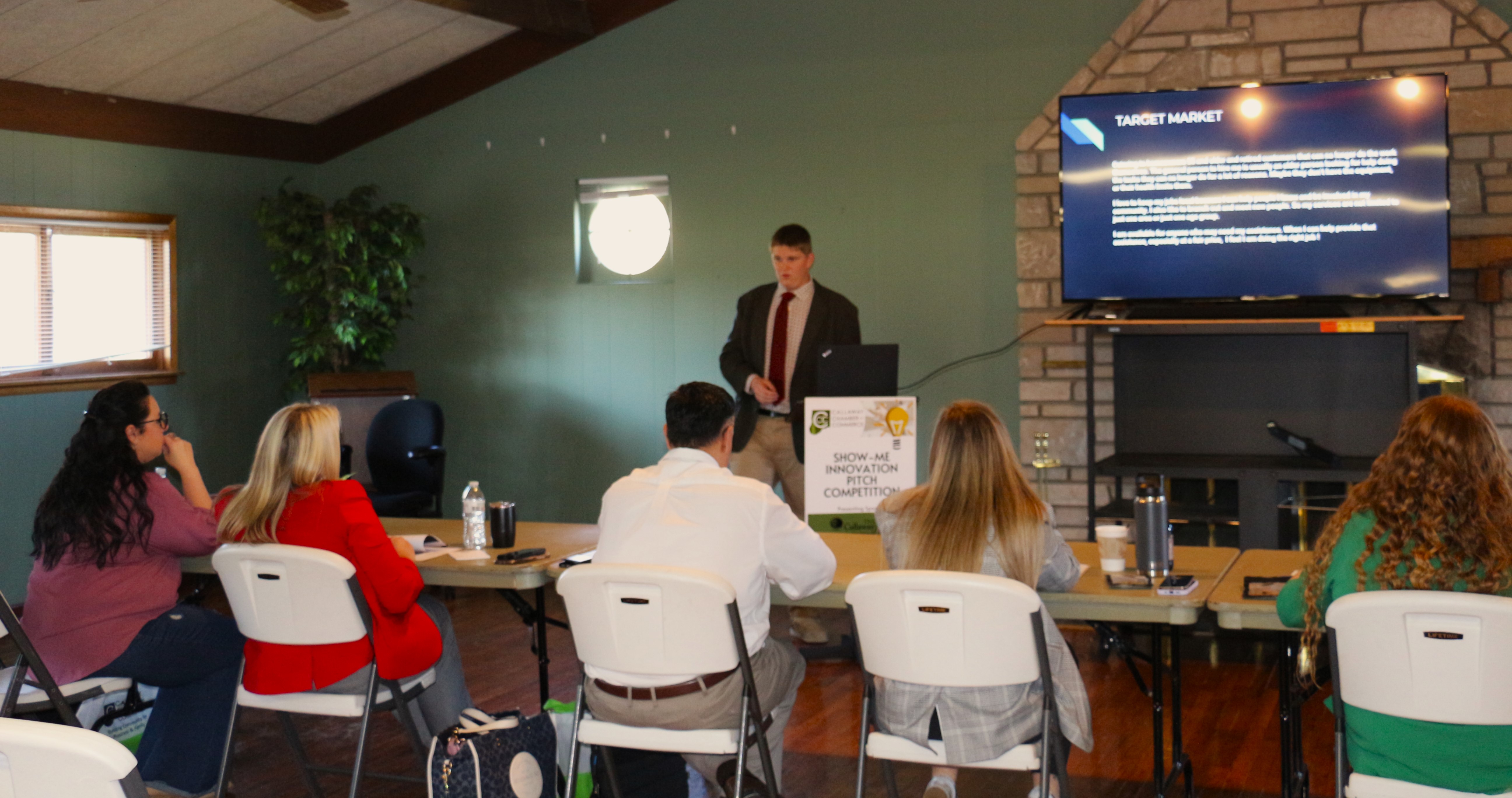 A young man in a suit stands before 5 judges pitching his business idea