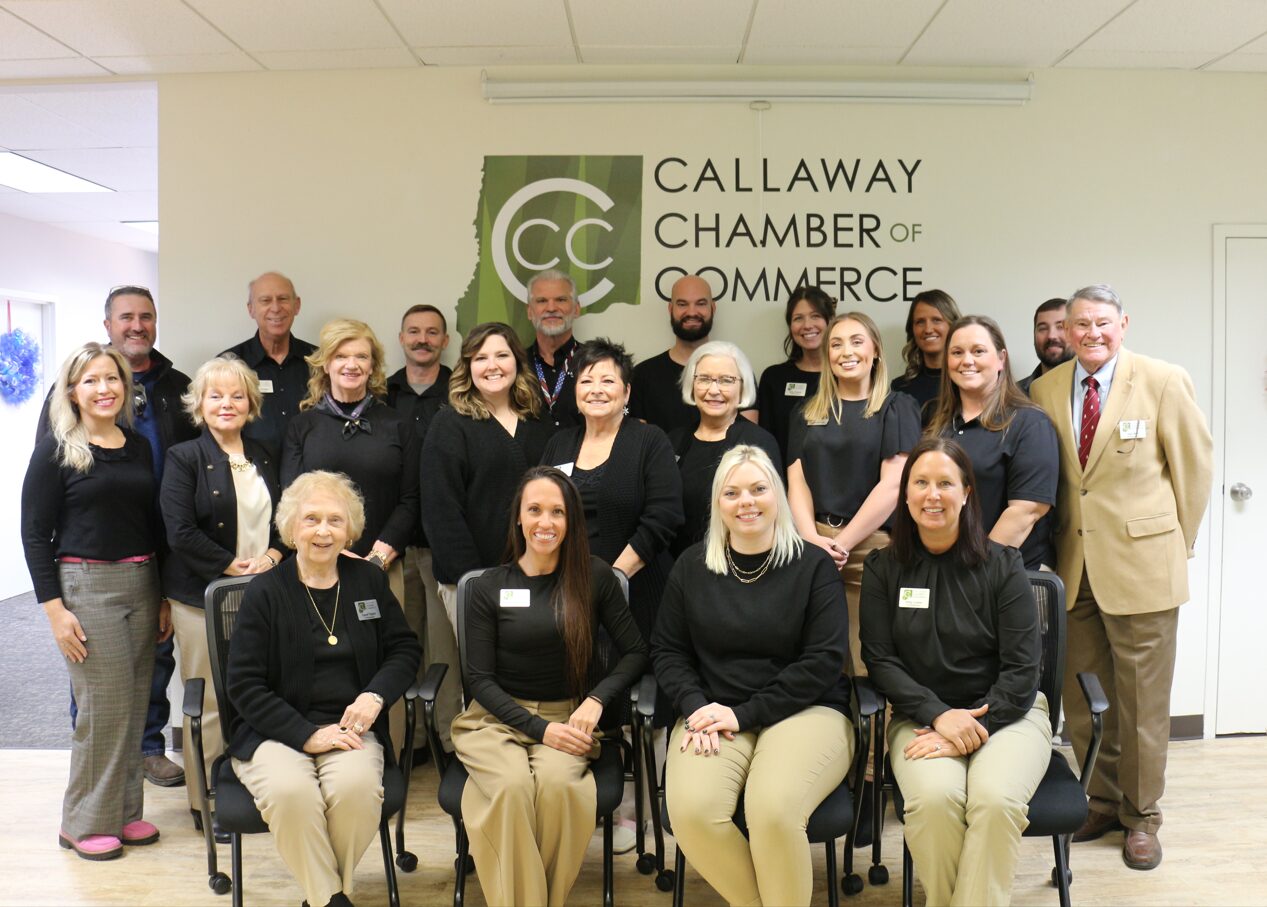 A group of people in black shirts and Chamber nametags stand in front of a wall with the Callaway Chamber of Commerce logo
