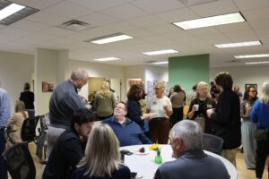 Groups of people mingle in an open space. Some are holding plates of breakfast or cups of coffee