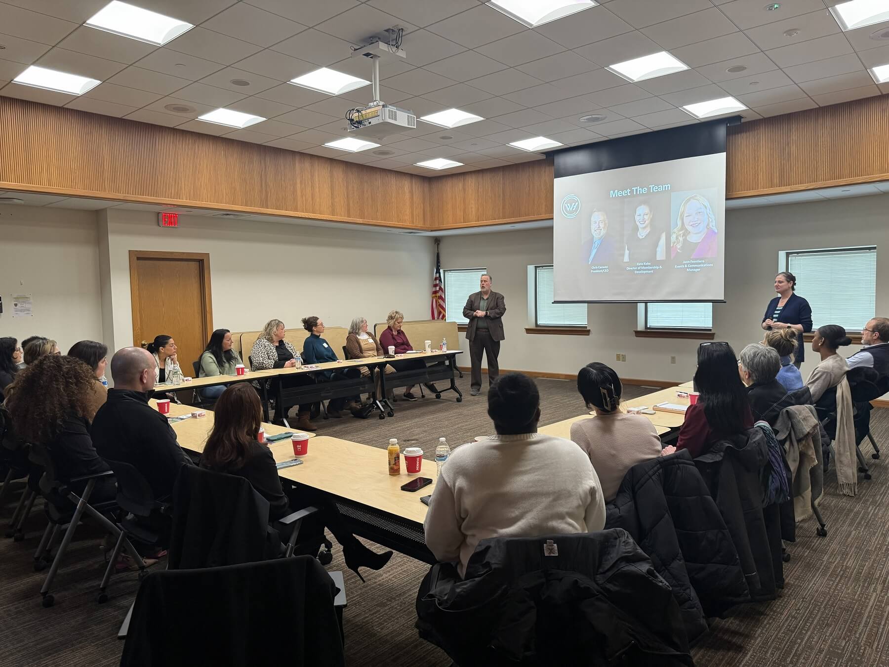 Man and woman presenting In front of a screen to a room of people at a table